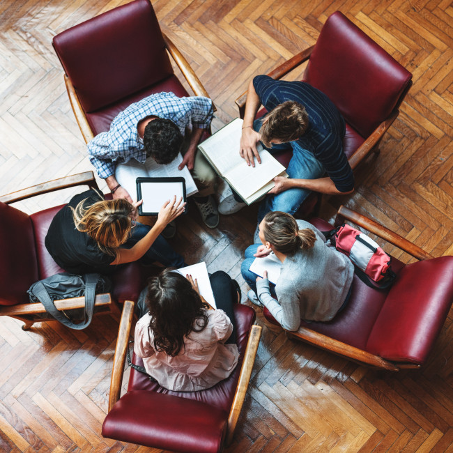 Five people sitting in a circle are working together and consulting documents and tablets in a modern office, symbolising the Group’s model of inclusive and sustainable governance